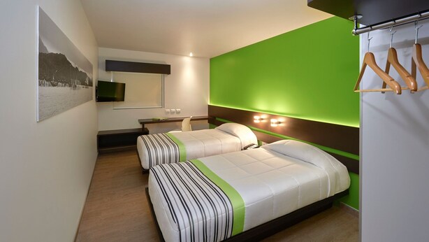 Ein modernes Hotelzimmer mit zwei Betten, einer grünen Akzentwand, einem Wand-Fernseher und einem hölzernen Kleiderhaken.