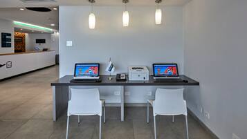A reception desk with two laptops, a phone, and a printer. There are two white chairs in front of the desk.
