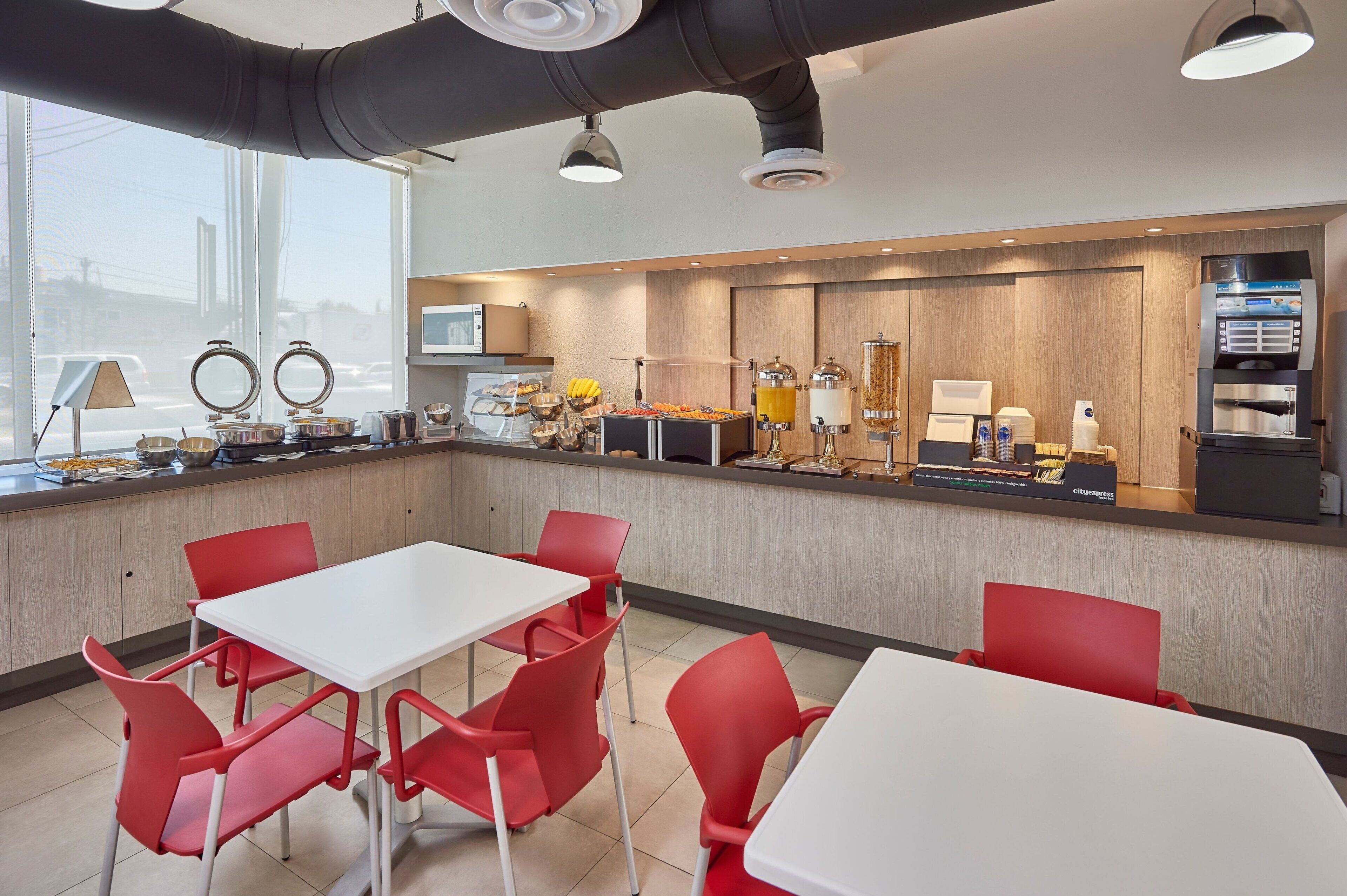 A modern breakfast area with a counter, red chairs, and a white table.