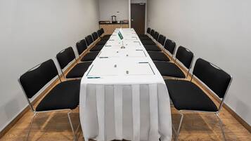 Un salón de conferencias con una larga mesa, sillas negras y un mantel blanco.