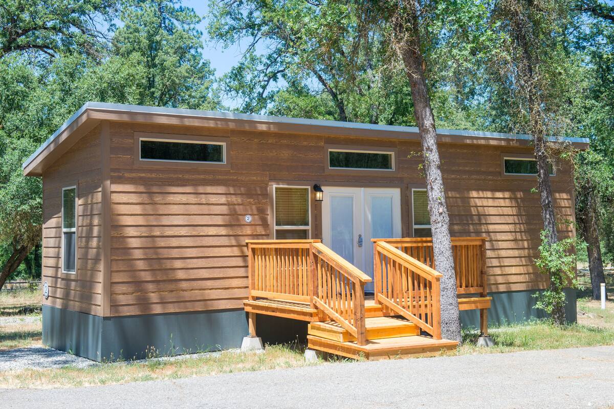 A two-story cabin with a wooden exterior, a front porch with wooden railings, and a door with a window above it.