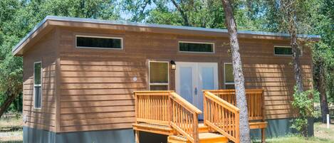 A two-story cabin with a wooden exterior, a front porch with wooden railings, and a door with a window above it.