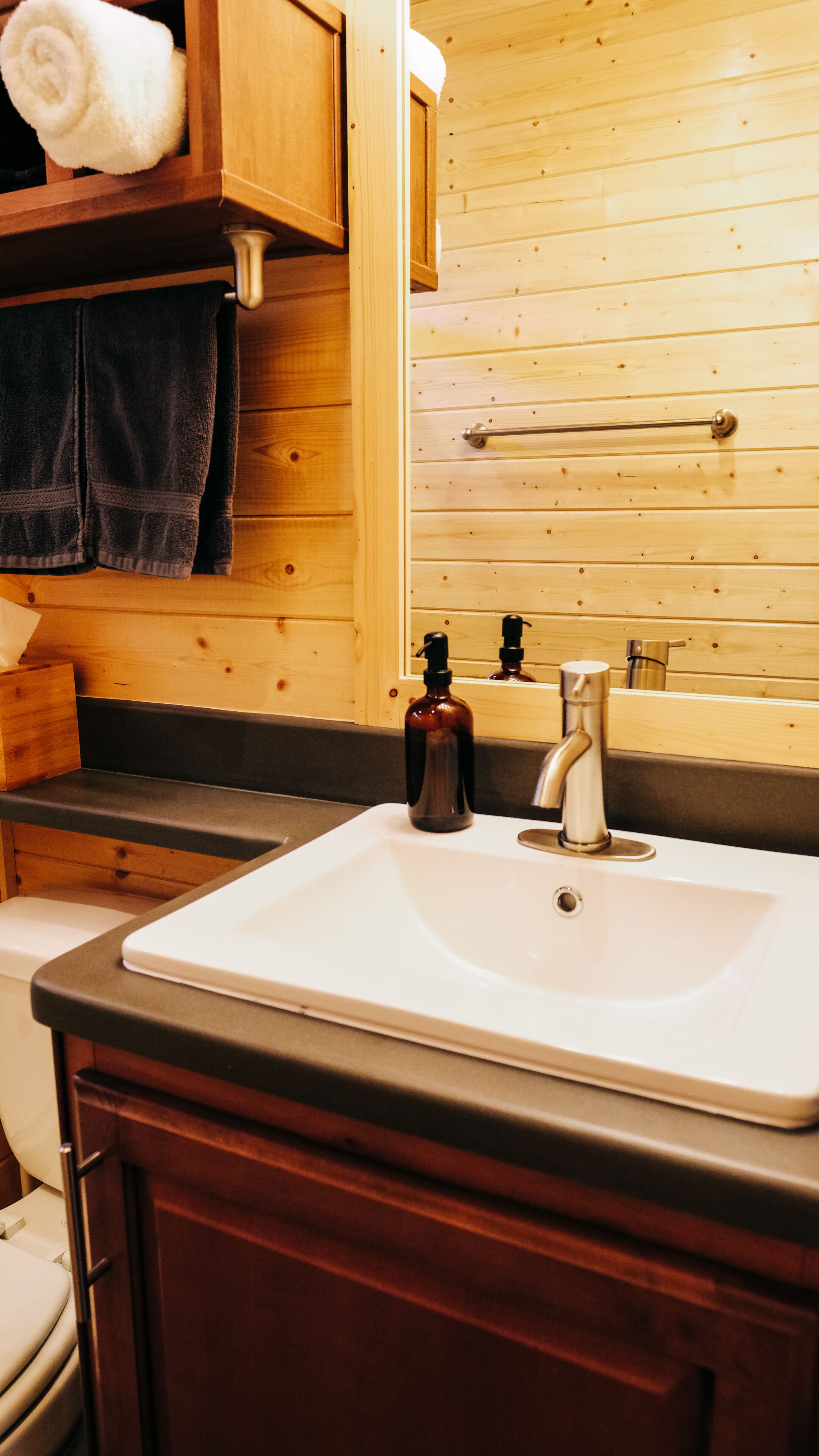 A bathroom with a wooden vanity, a white sink, a mirror, and a towel rack.