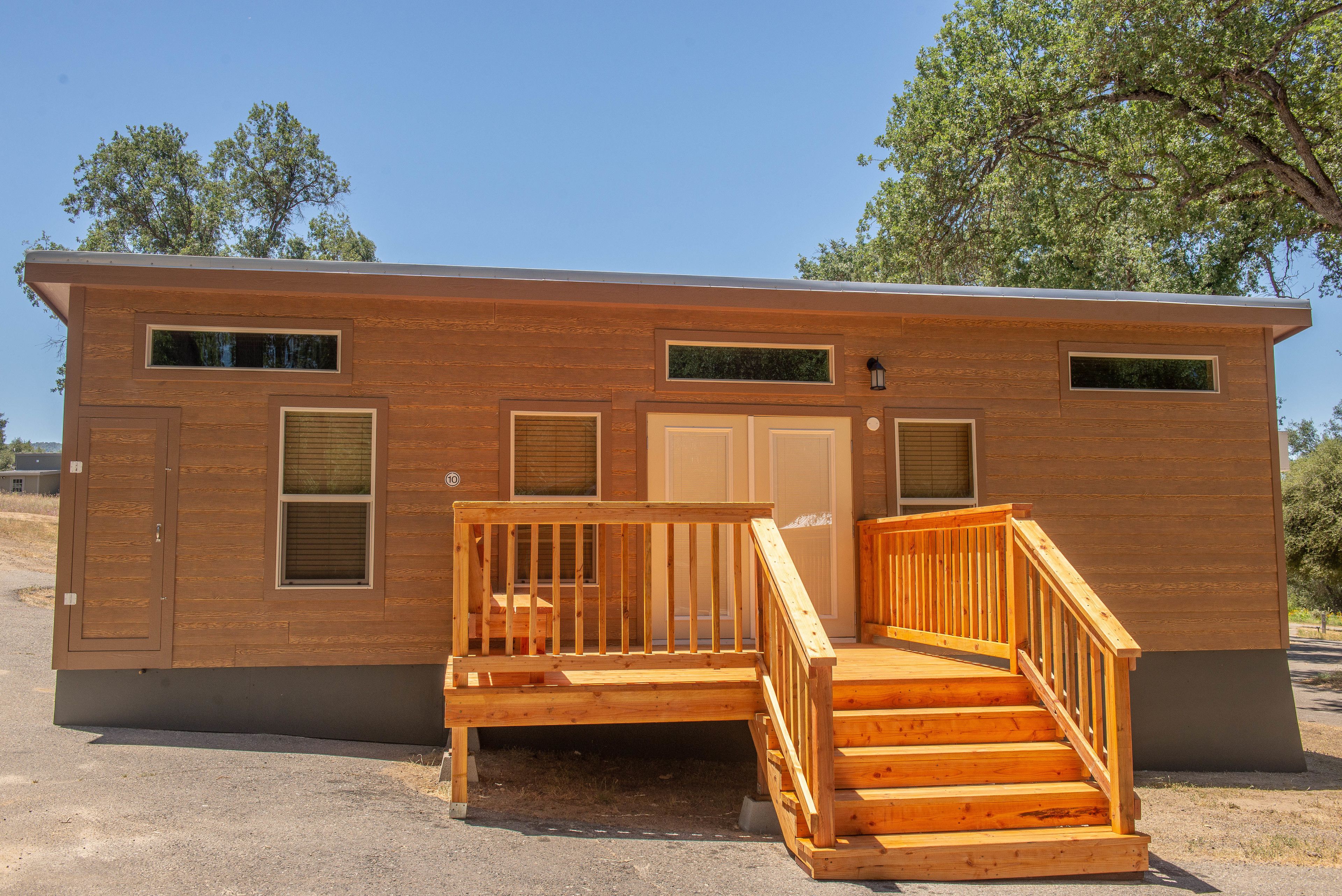 A single-story wooden cabin with a front porch, a small deck, and a door.