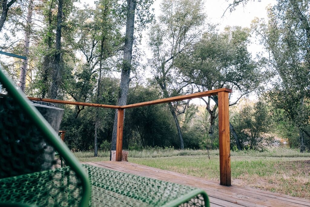 A wooden deck with a metal railing, surrounded by trees.
