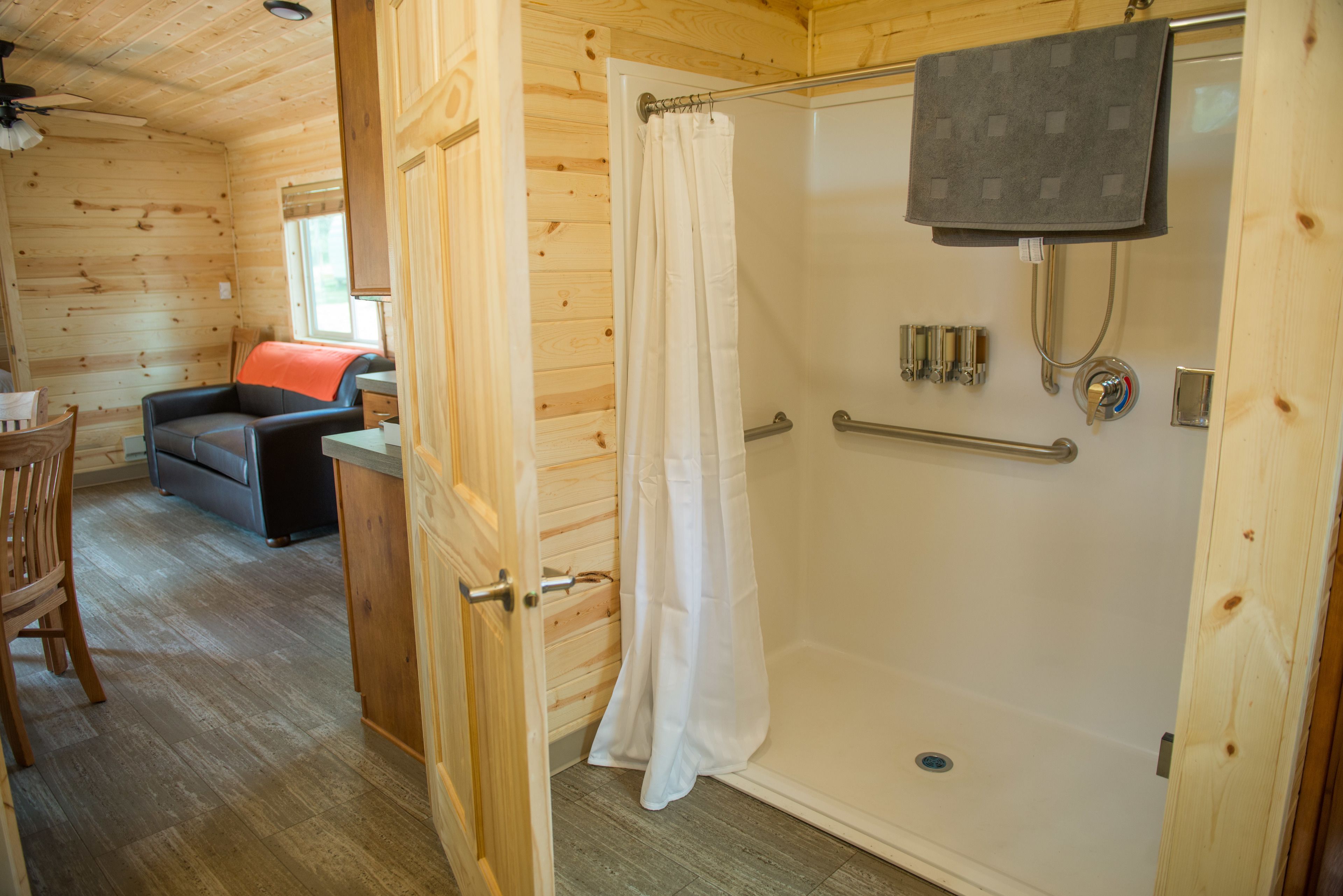 Interior de uma cabana de madeira com chuveiro, sofá e área de jantar.