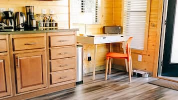 A wooden interior with a kitchen area, a dining table with a magazine, and a pet feeding station.