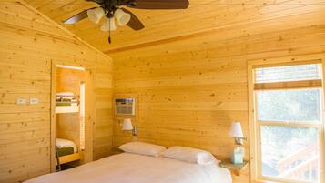 Une chambre dans une cabane en bois, avec un lit superposé, un ventilateur de plafond, une fenêtre donnant sur un paysage agréable et une lampe de chevet.