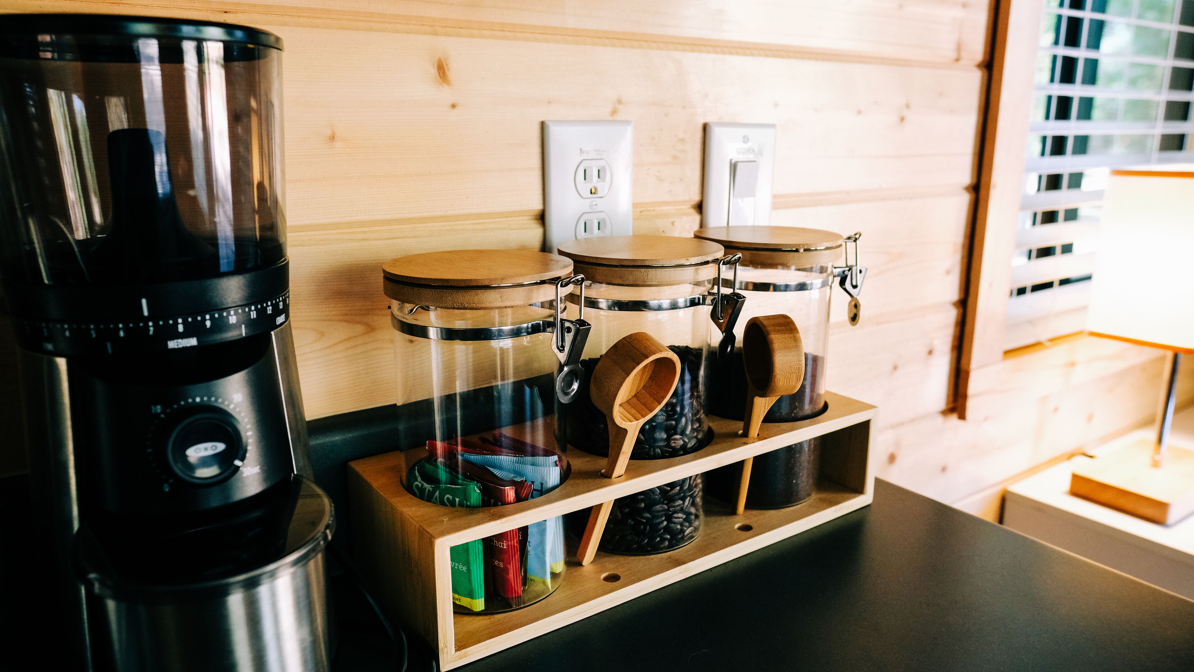 En köksdel med en kaffebryggare, burkar och träredskap på en hylla av trä.