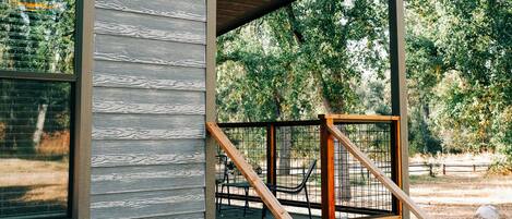 Un edificio moderno con fachada de madera, un porche cubierto con escaleras de madera y vistas a árboles al fondo.