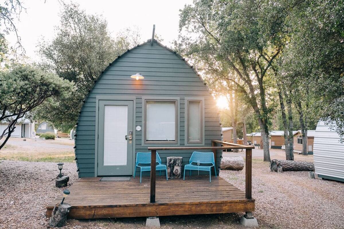 A small, single-story cabin with a porch, two chairs, and a table.