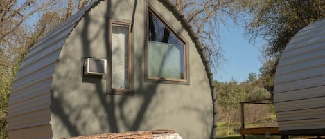 A small, single-story cabin with a window and a door, surrounded by trees.