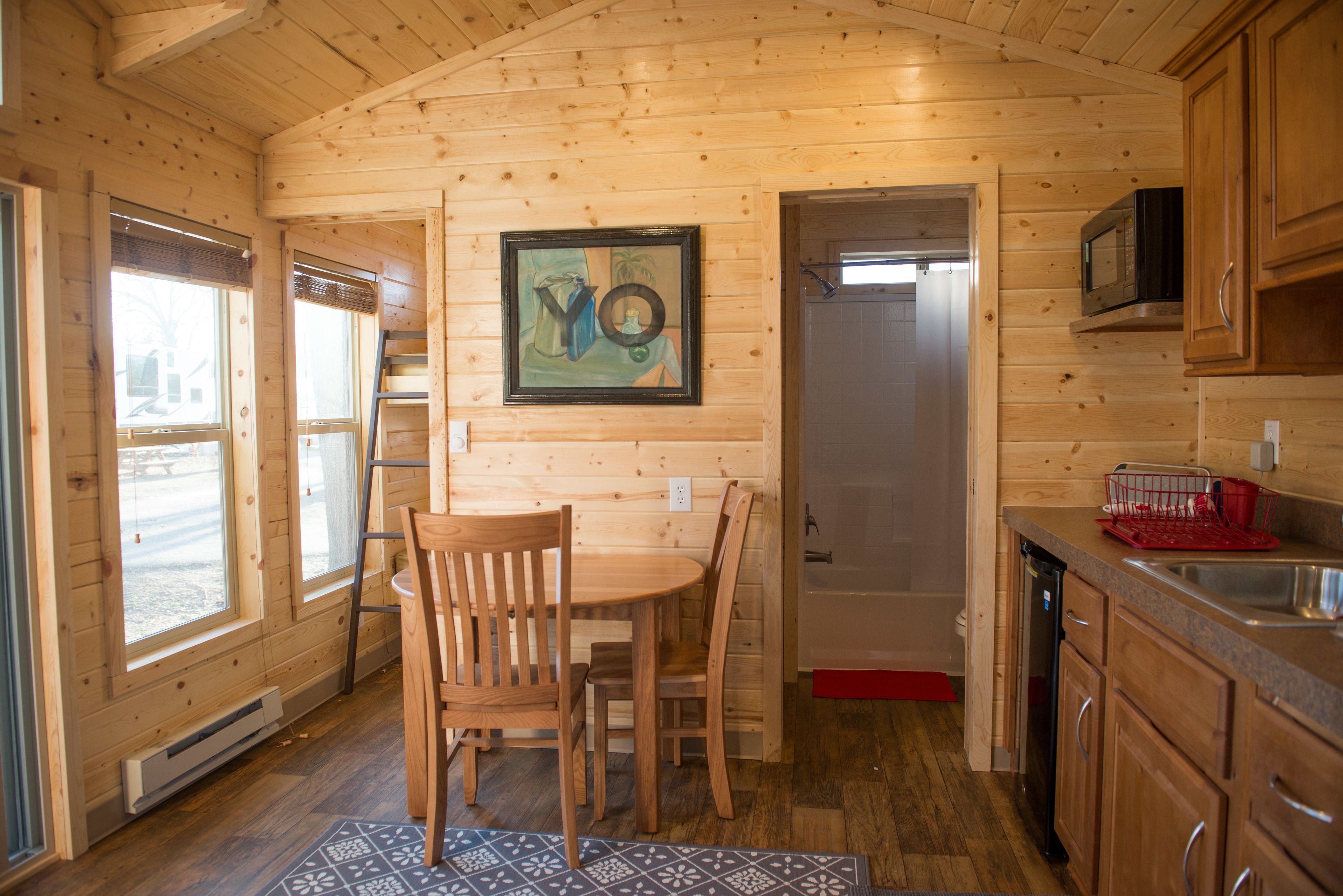 A wooden cabin interior with a dining area, kitchen, and a door leading to another room.