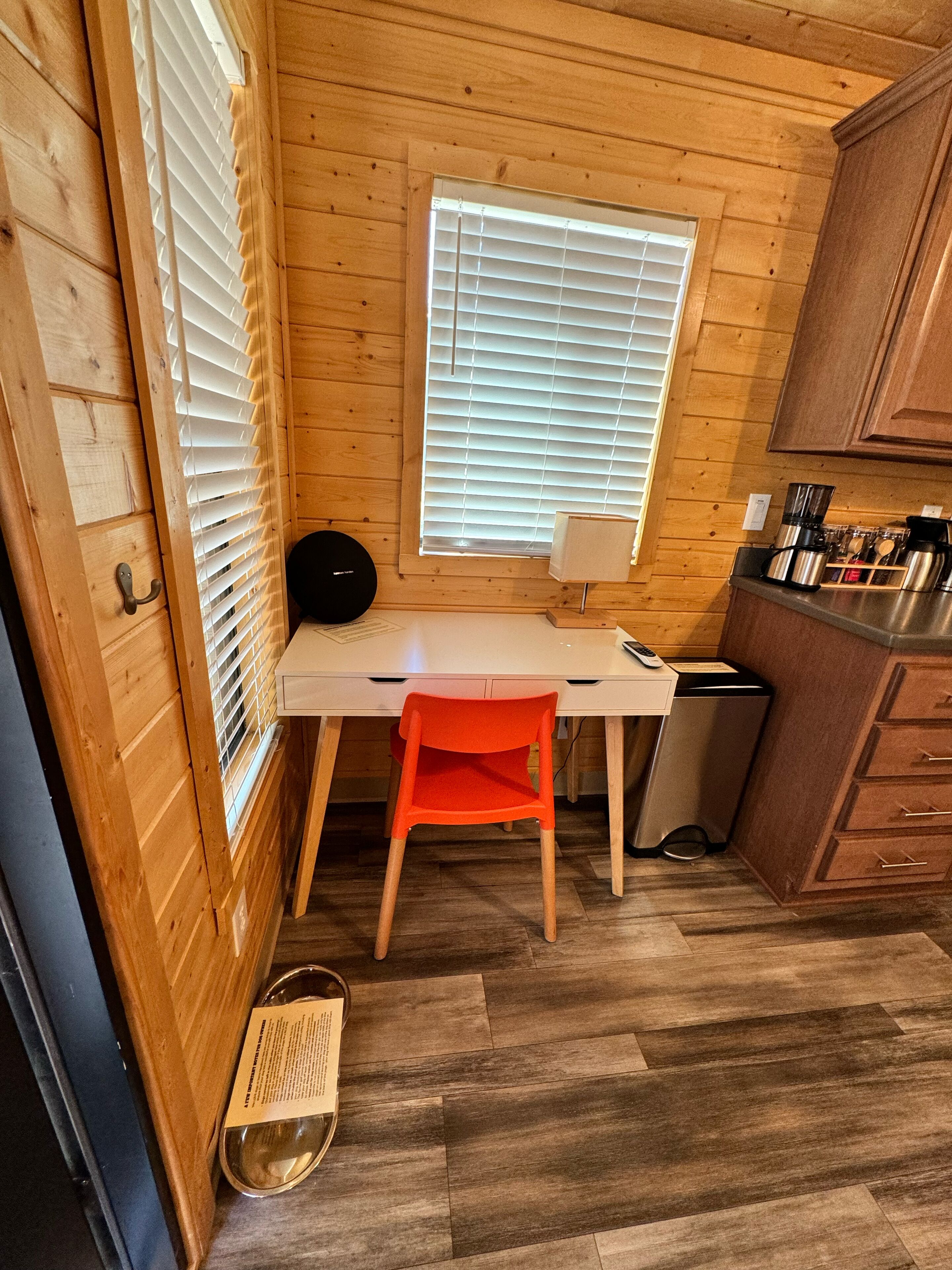 A compact kitchen with wooden walls, a white countertop, a sink, and a window with blinds.