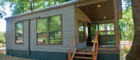 A modern cabin with a covered porch, large windows, and a wooden staircase leading to the entrance.