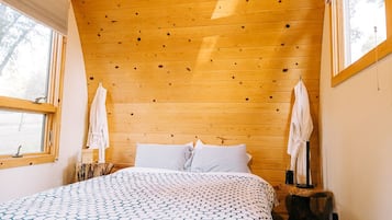 Un dormitorio con paneles de madera, una cama, dos ventanas y una mesita.