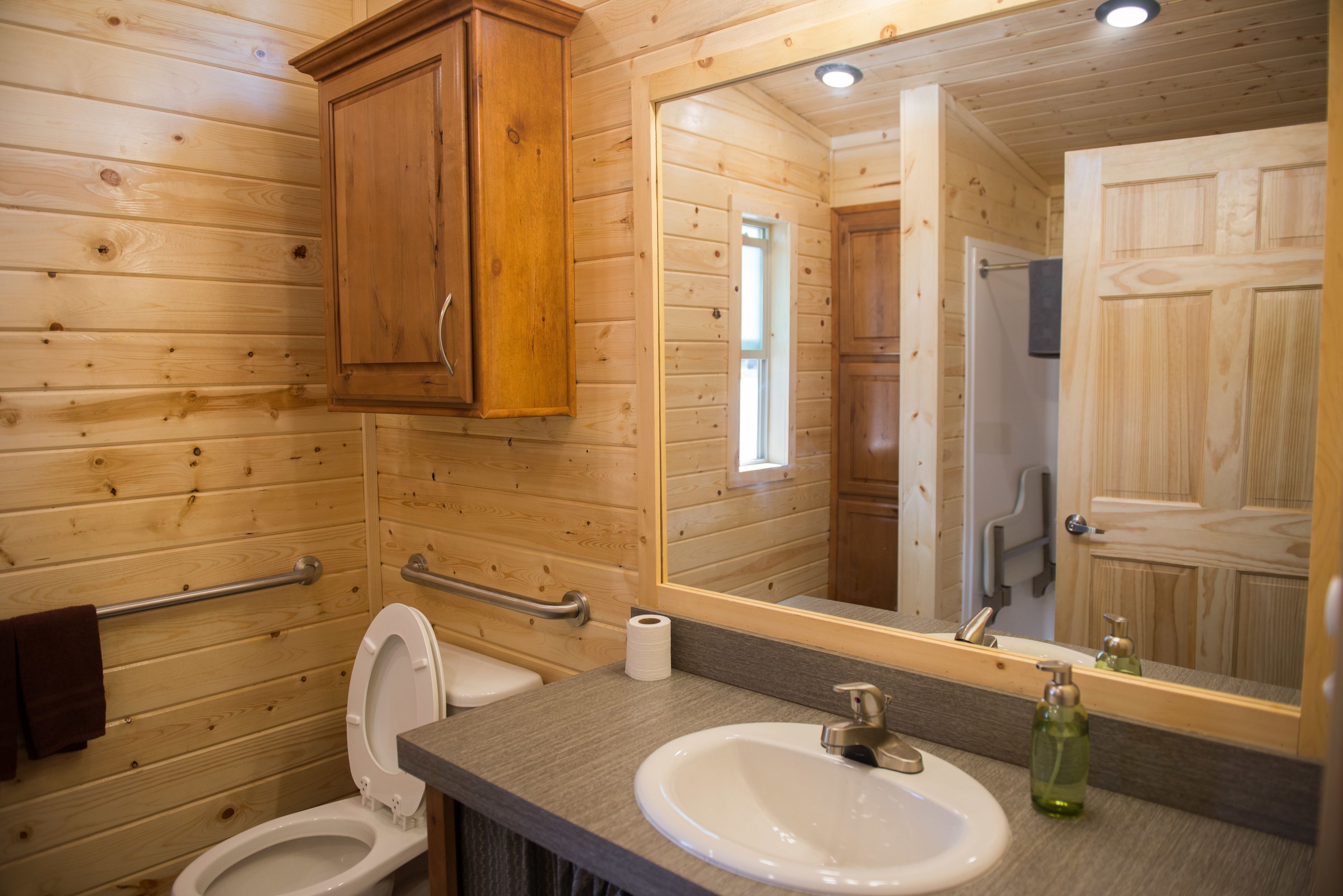 A wooden cabin bathroom with a toilet, sink, and mirror.