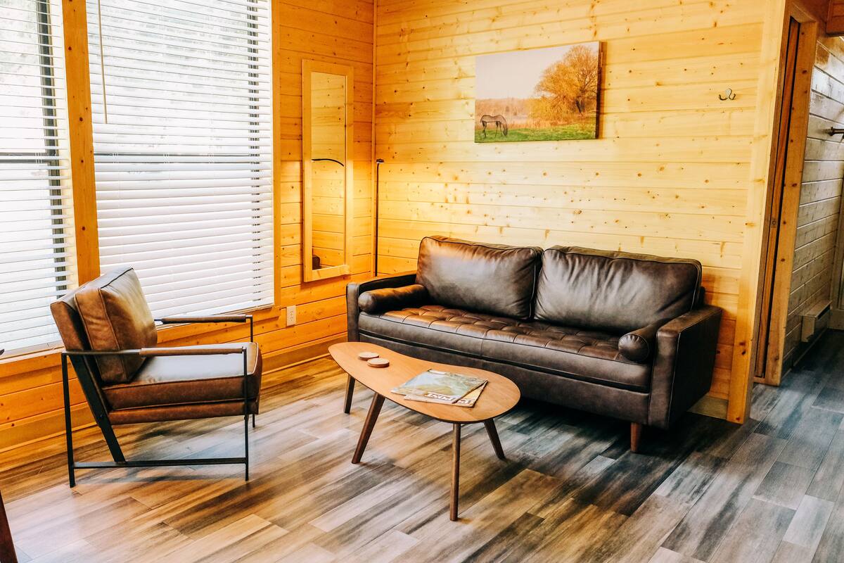 A cozy room with a wooden interior, a leather sofa, a wooden table, and a chair.