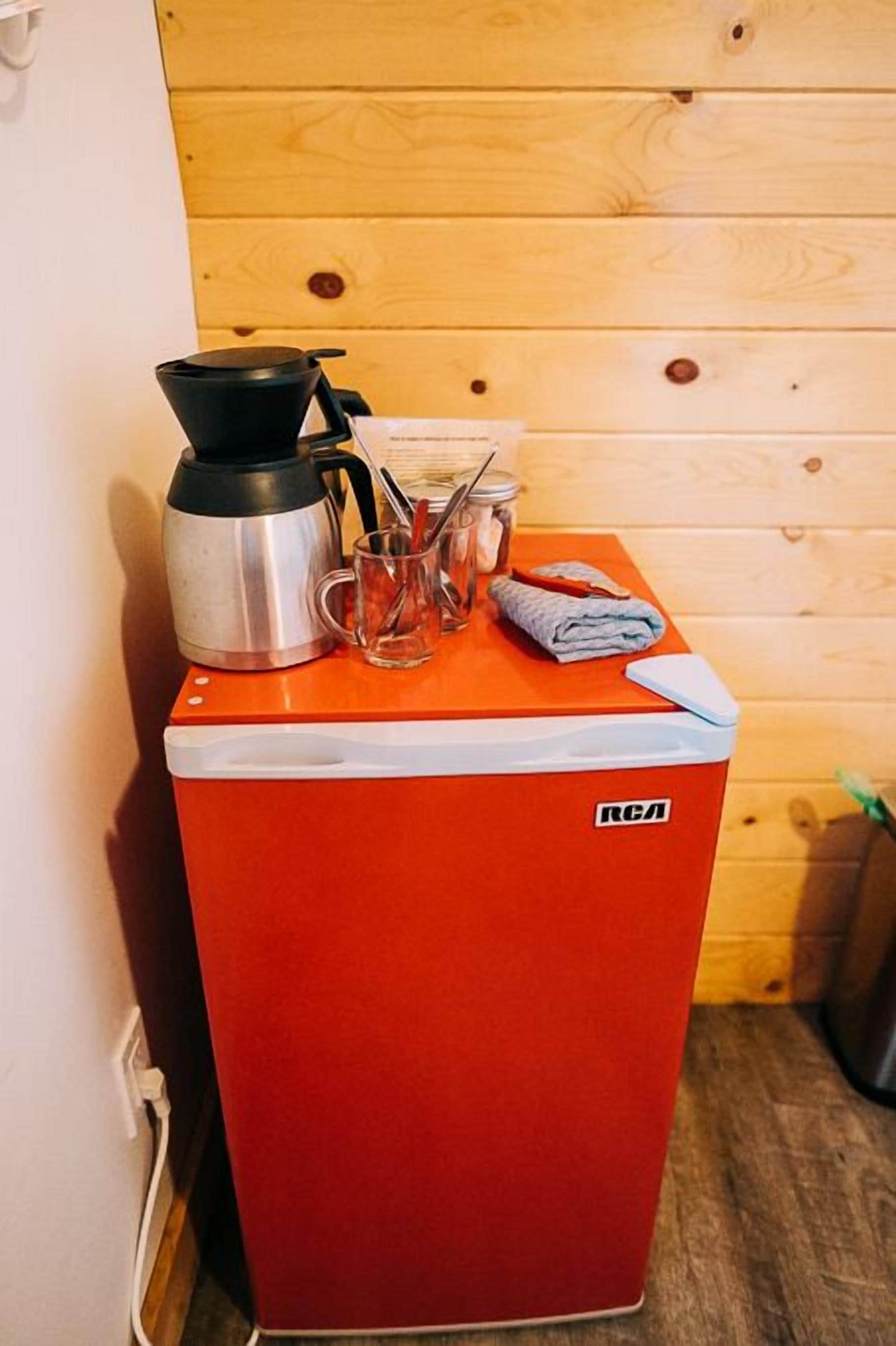 Uma geladeira vermelha e compacta, com uma cafeteira preta e uma caneca de vidro em cima.