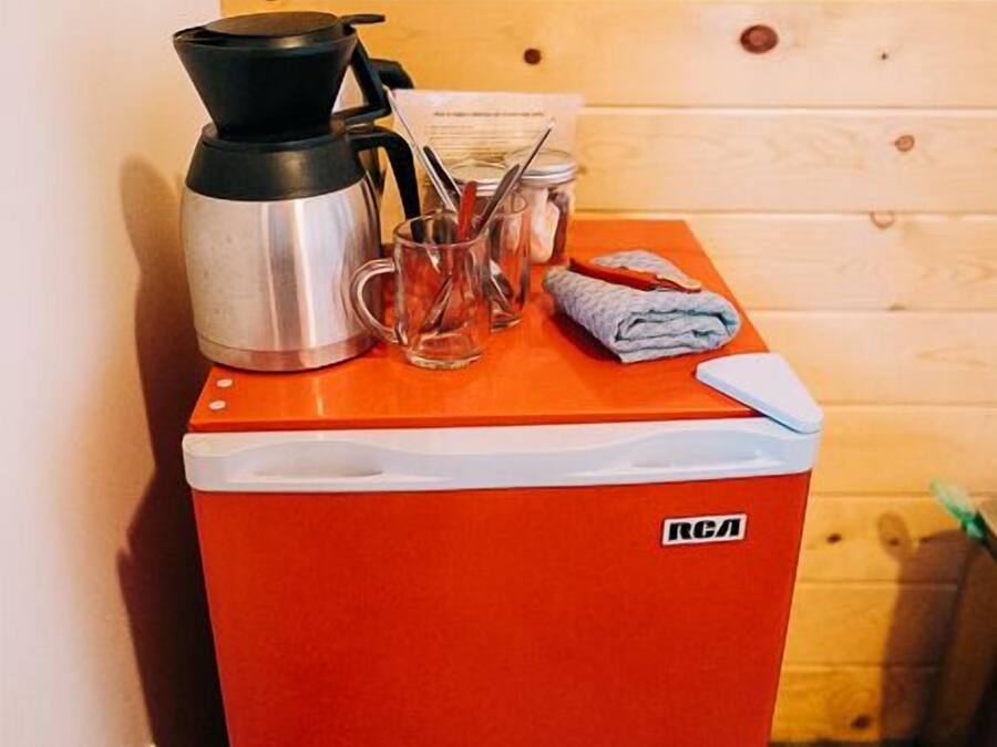 Uma geladeira vermelha e compacta, com uma cafeteira preta e uma caneca de vidro em cima.