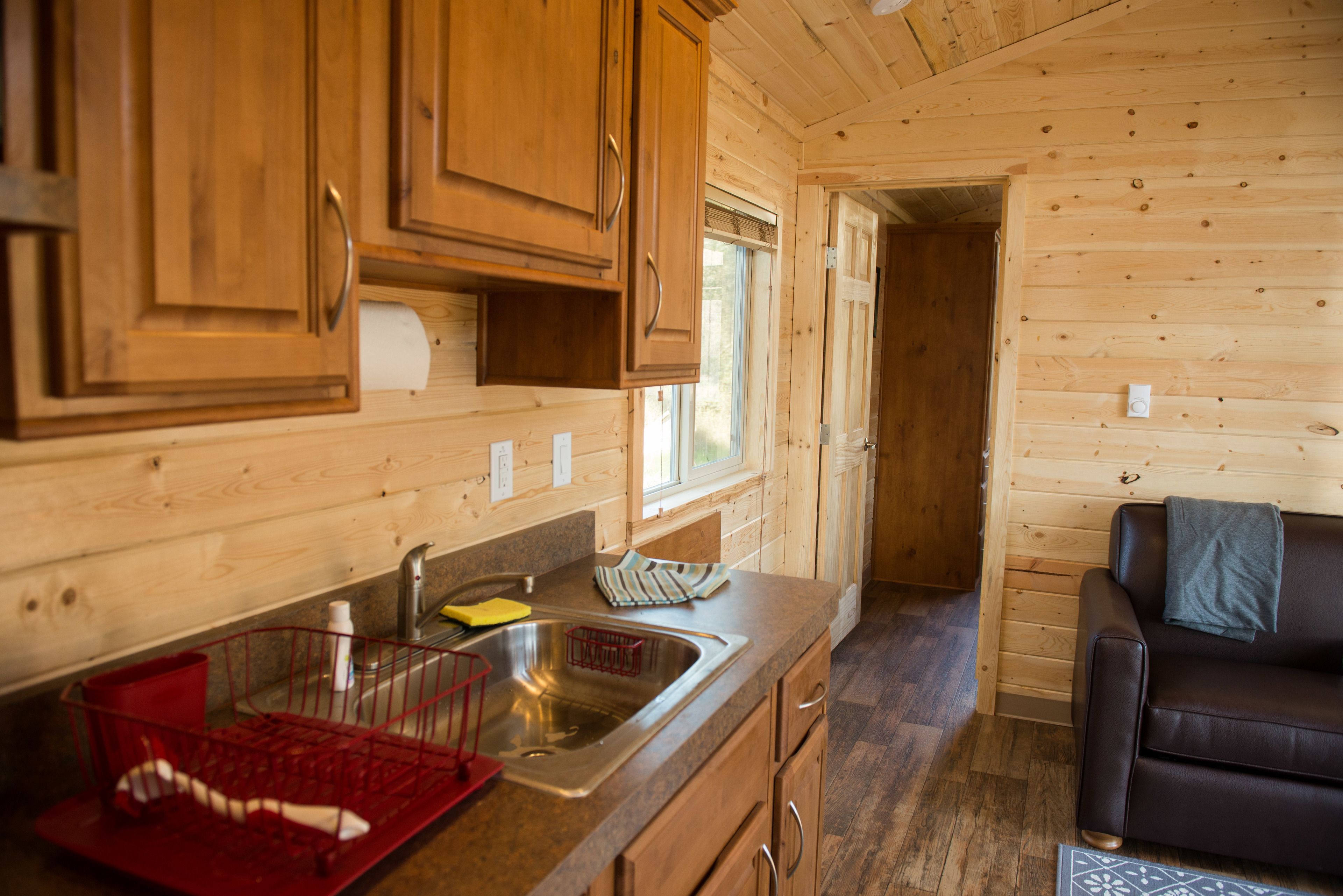 A wooden cabin interior with a kitchen area featuring a sink, cabinets, and a dining table.