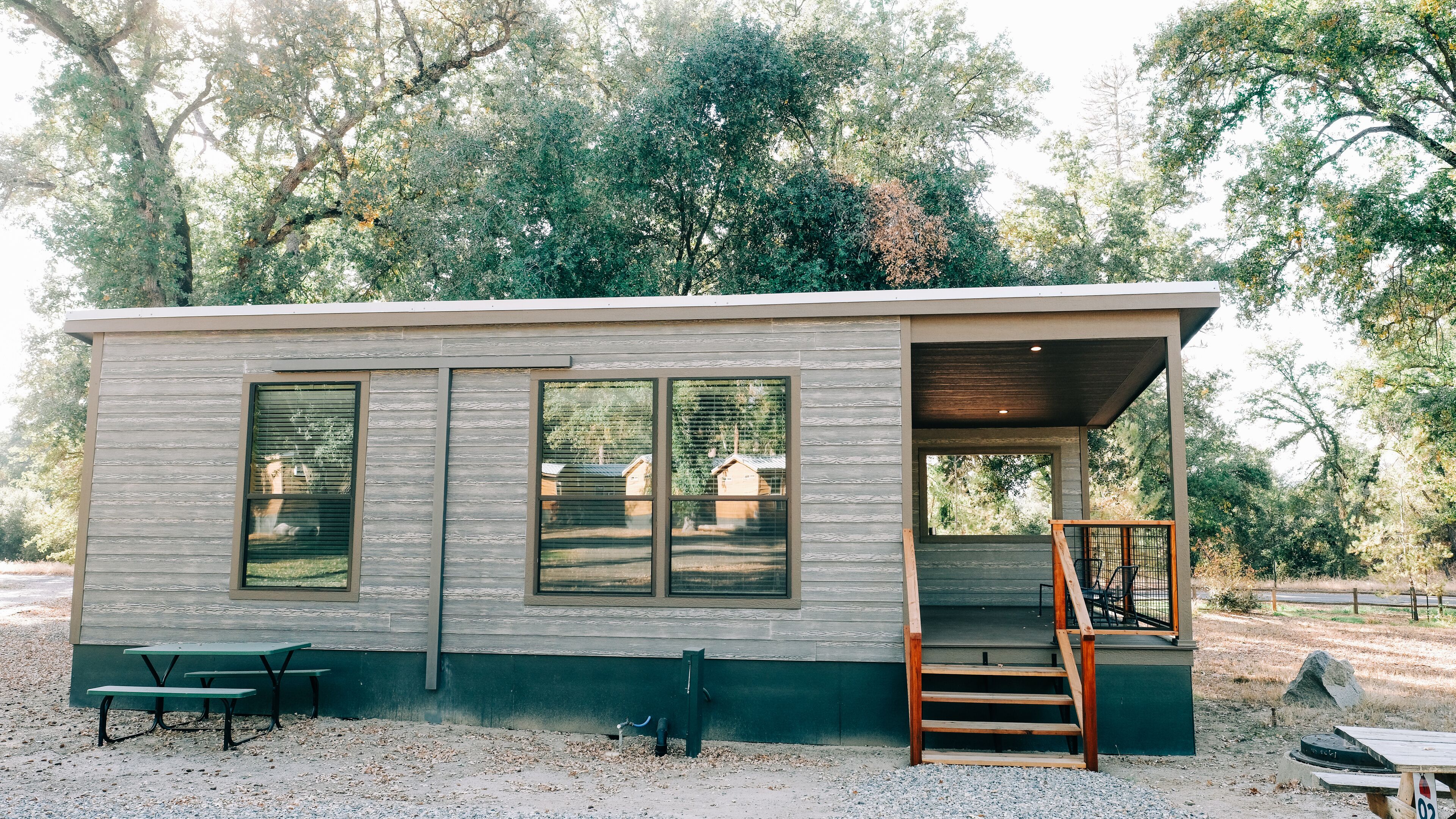 A small cabin with a covered porch, a wooden staircase, and a picnic table.