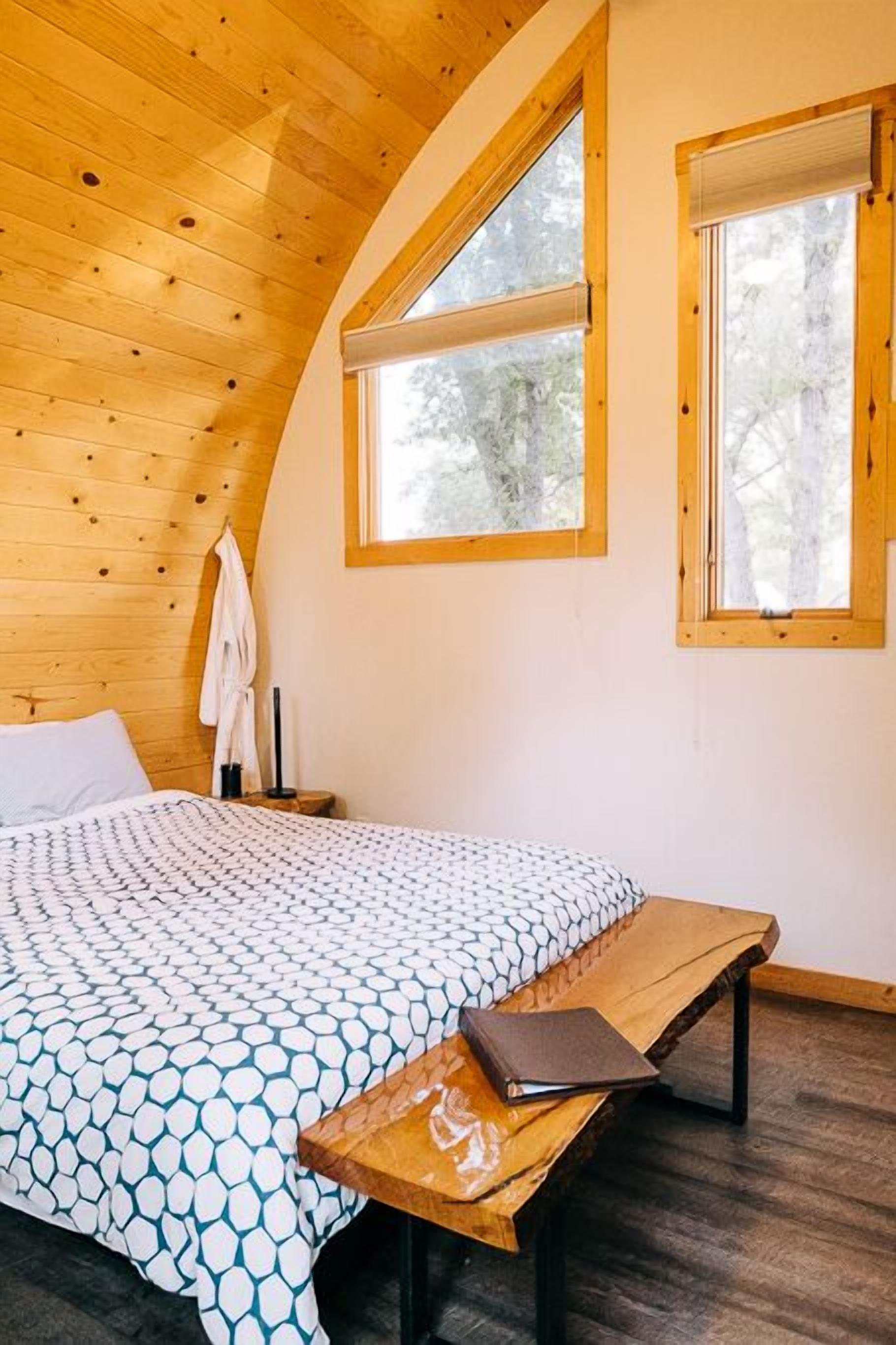 Un dormitorio con una cama, un banco de madera y dos ventanas.