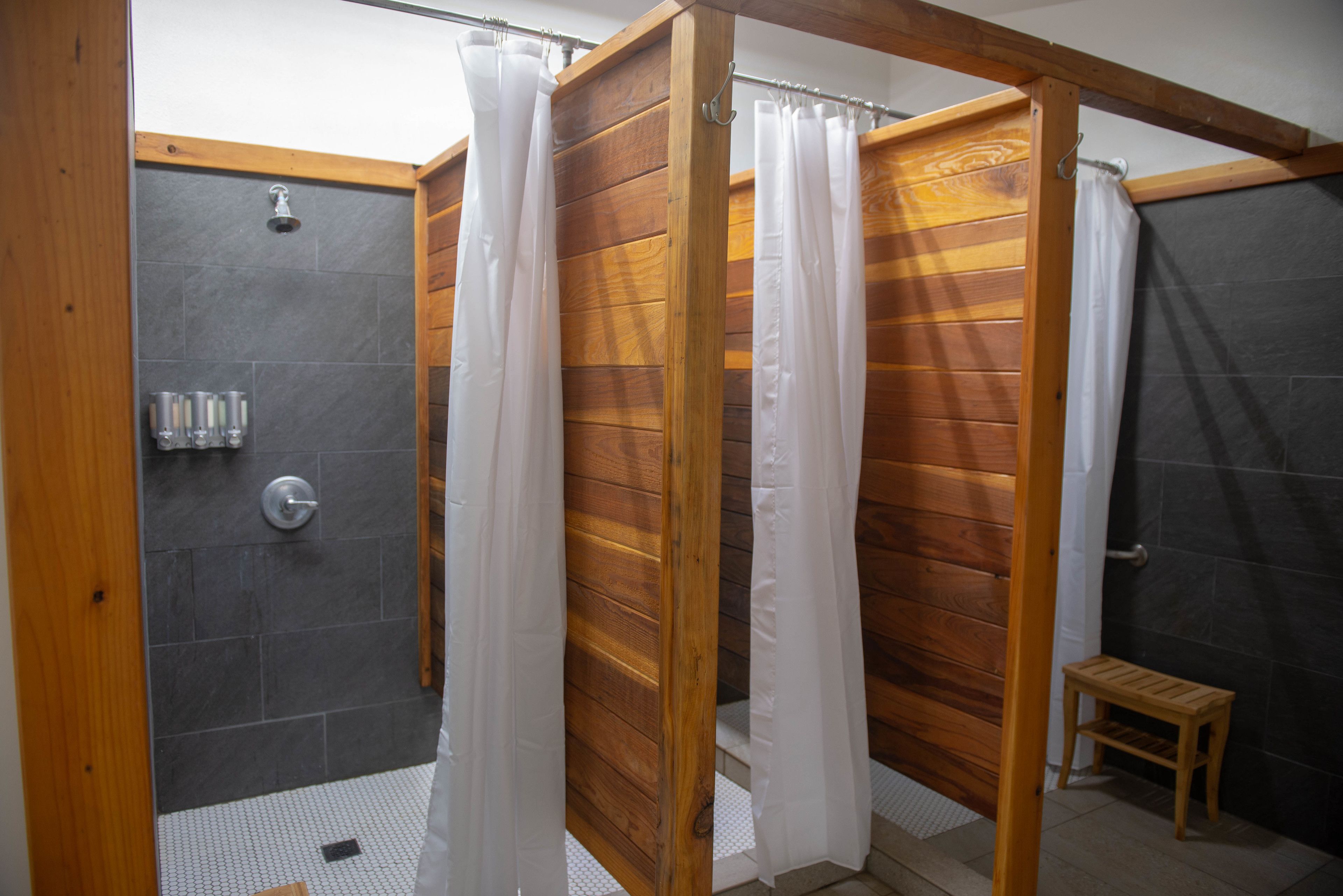 A shower area with a wooden partition, a small wooden stool, and a showerhead.