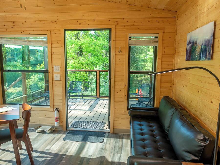 Ein Holzblockhaus-Innenraum mit Essbereich, einer Couch und großen Fenstern mit Blick auf den Wald.