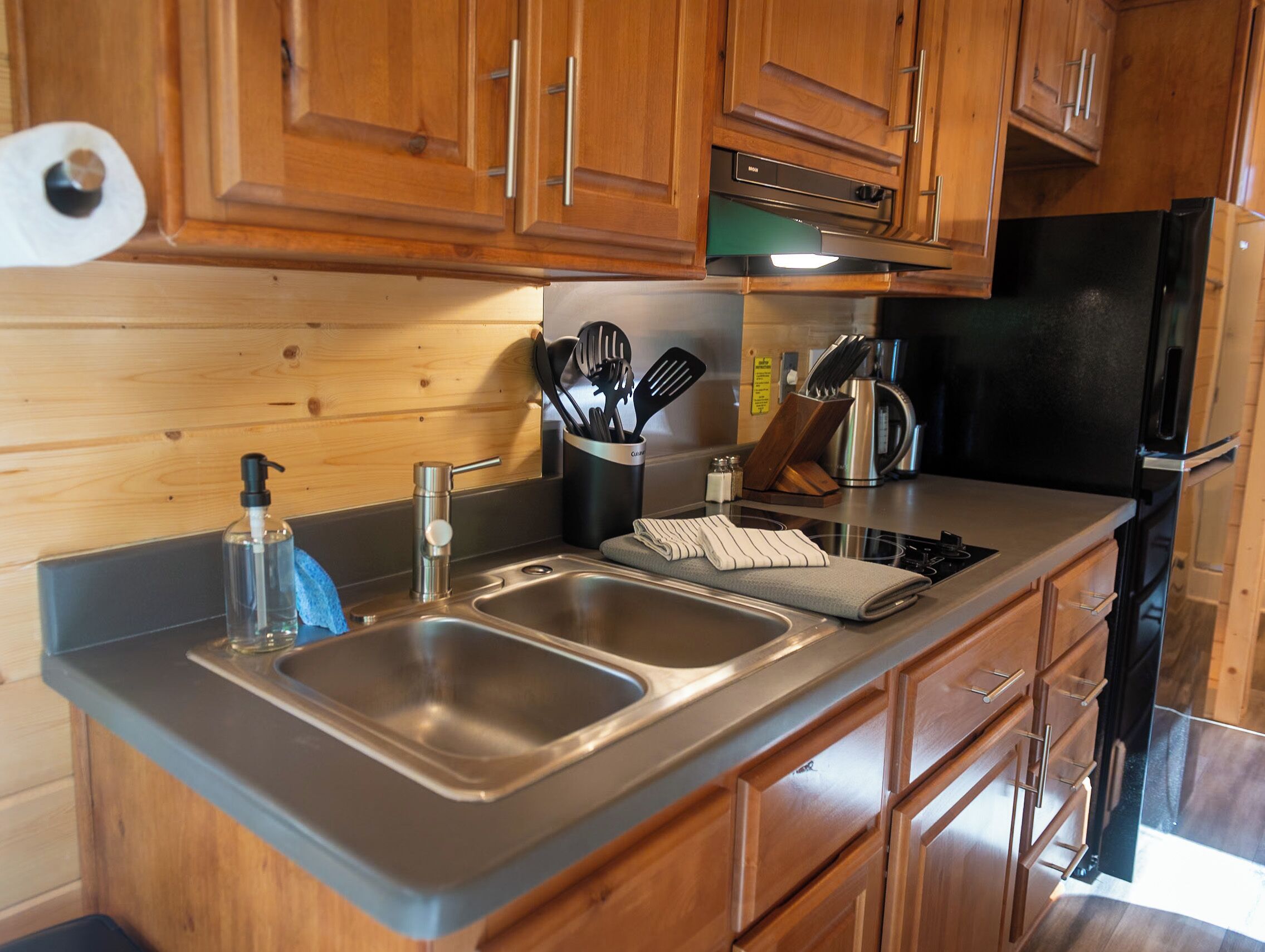 A modern kitchen with wooden cabinets, stainless steel sinks, and a black refrigerator.