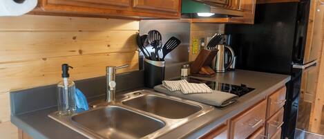 A modern kitchen with wooden cabinets, stainless steel sinks, and a black refrigerator.