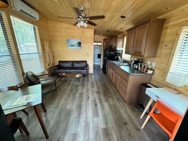 Un interior acogedor de cabaña con piso de madera, un sofá de cuero, una mesa de comedor y una zona de cocina.