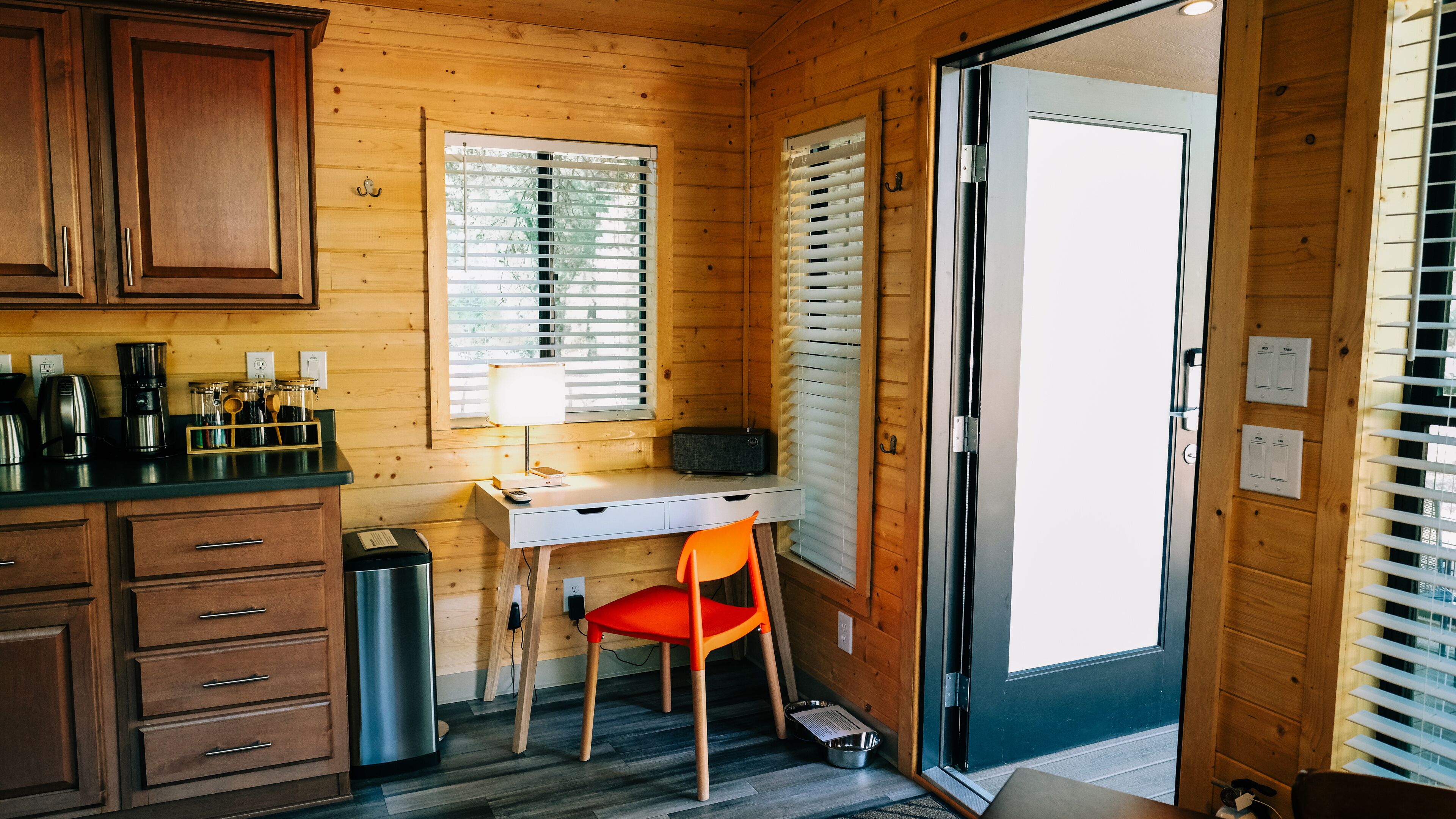 A compact kitchen with wooden cabinets, a countertop with a coffee maker, a sink, and a window with blinds.