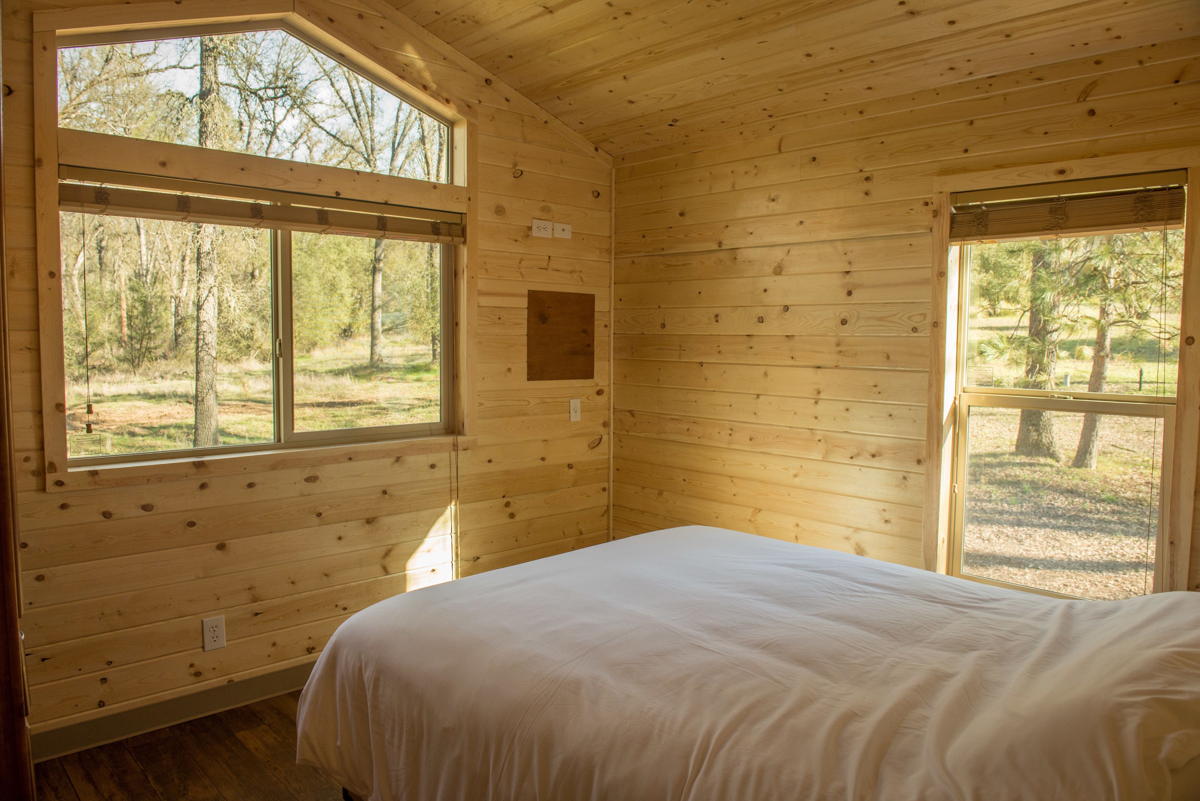 A wooden cabin bedroom with a bed, large windows, and a view of the outdoors.