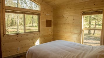 A wooden cabin bedroom with a bed, large windows, and a view of the outdoors.