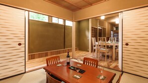 Una habitación tradicional japonesa con suelo de tatami, una mesa de madera para comer y sillas, y puertas correderas.