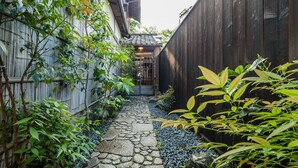 Un sendero de piedra que conduce a una puerta tradicional japonesa, rodeado de bambú y otra vegetación.