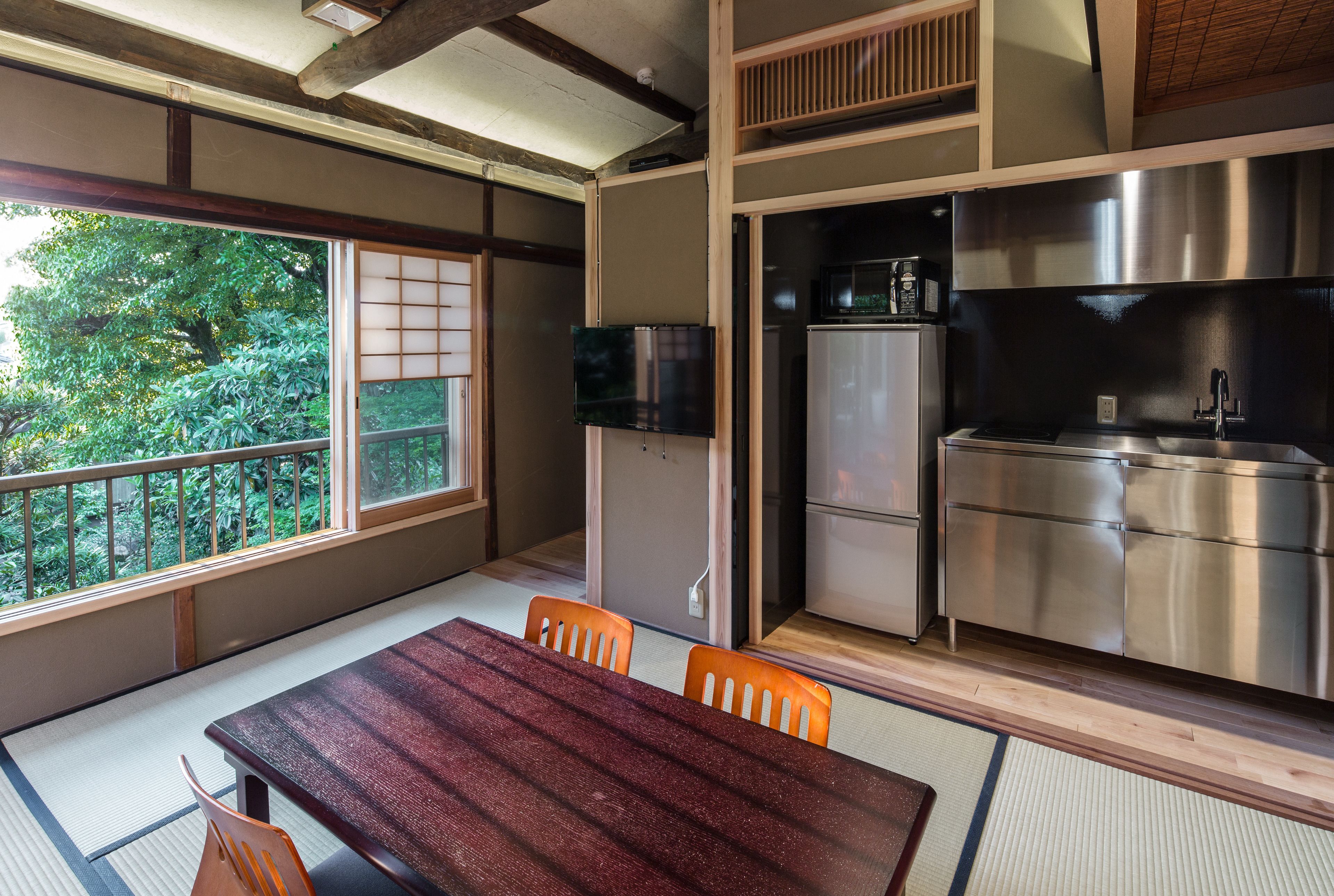 A traditional Japanese-style room with tatami flooring, a wooden table, and a view of greenery outside.