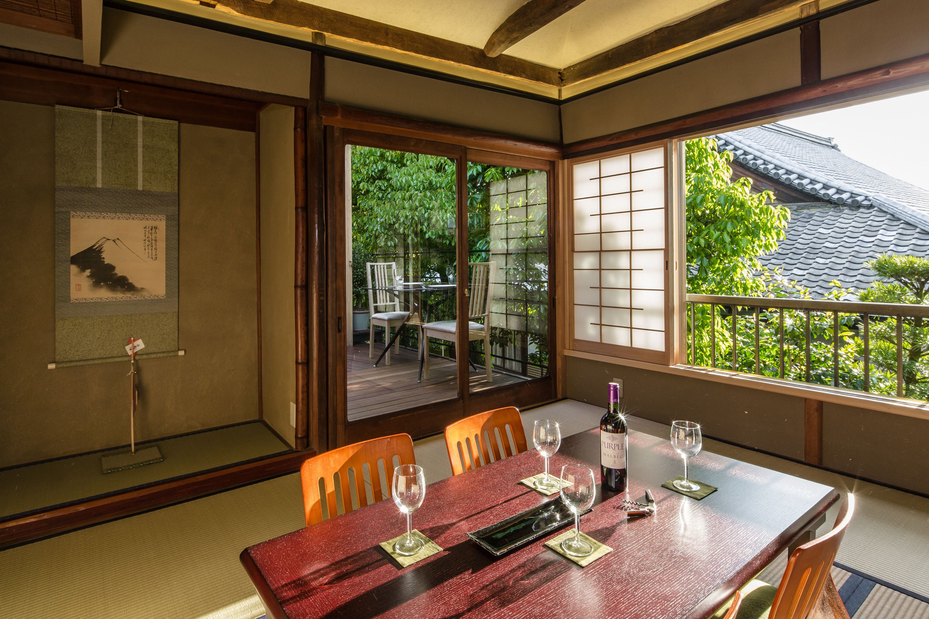 A traditional Japanese-style room with tatami flooring, a wooden table with glasses and a bottle, and sliding doors leading to an outdoor deck.