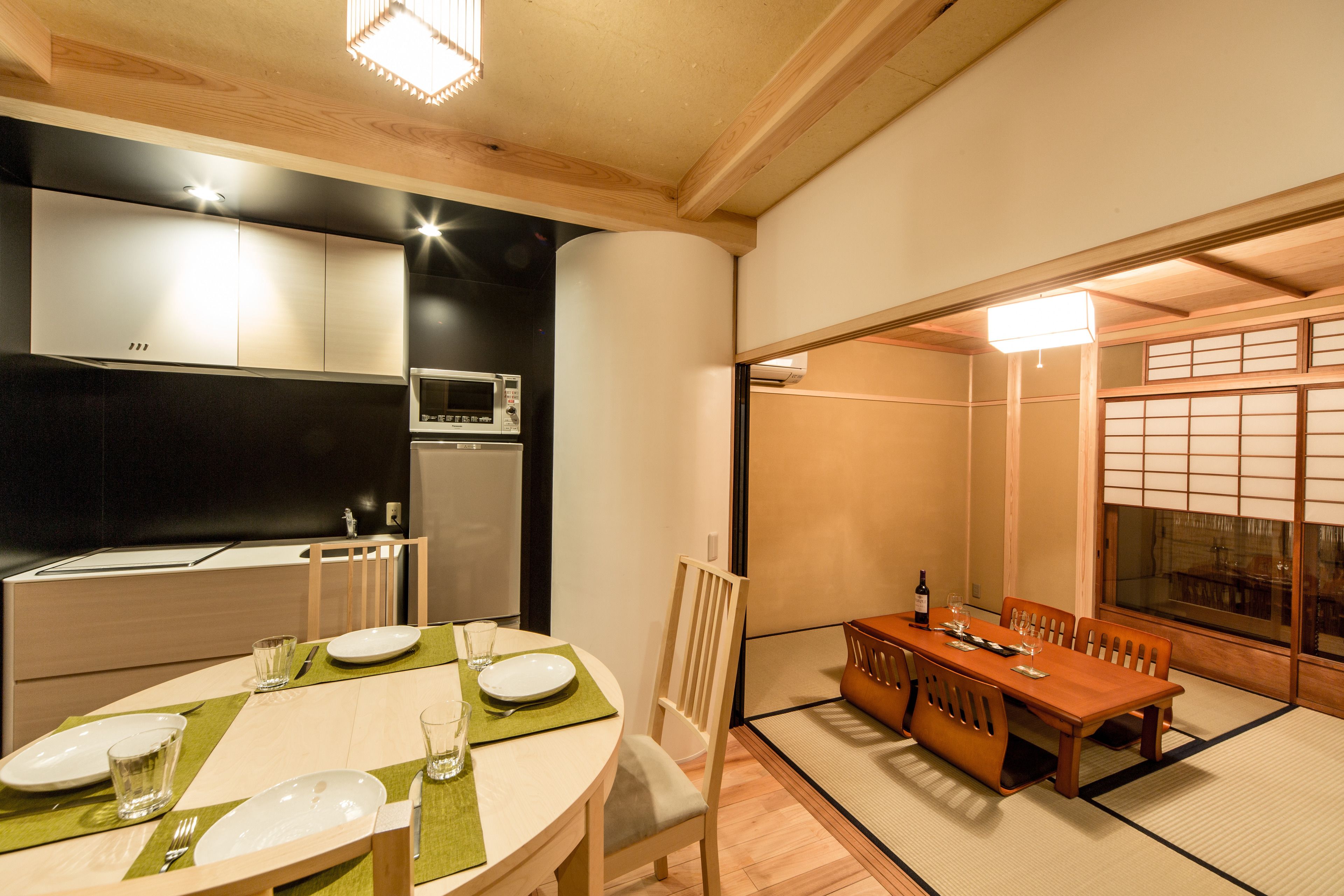 A traditional Japanese-style dining room with tatami mats, a wooden table, and a view of a garden through a shoji screen.
