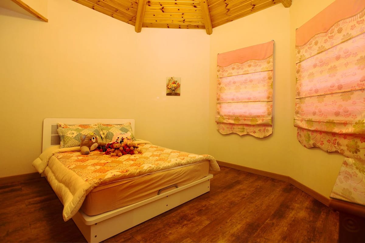 Une chambre avec un plafond en bois, un lit recouvert d’une couvre-lit à motifs floraux et des rideaux à fleurs.