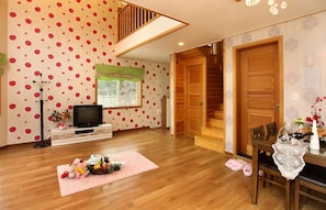Una sala de estar con televisor, piso de madera, una escalera y un comedor con mesa y sillas.