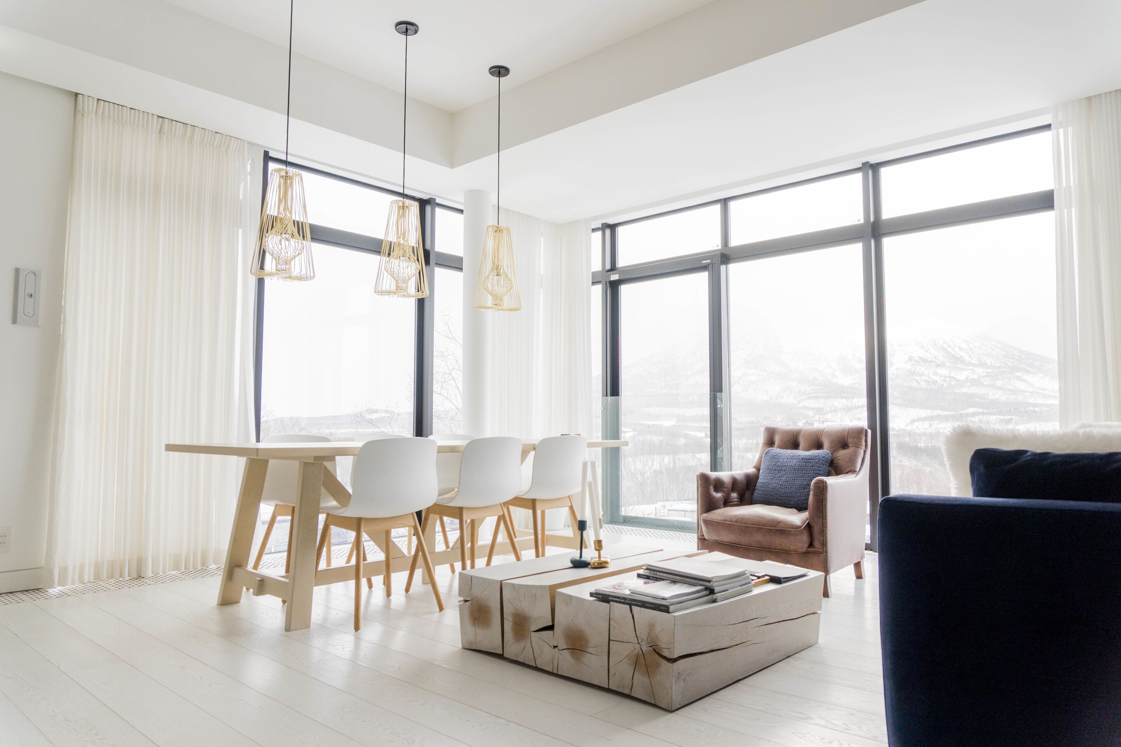 A spacious living room with a large window, a dining area with a wooden table and chairs, and a cozy seating area with a sofa and armchair.