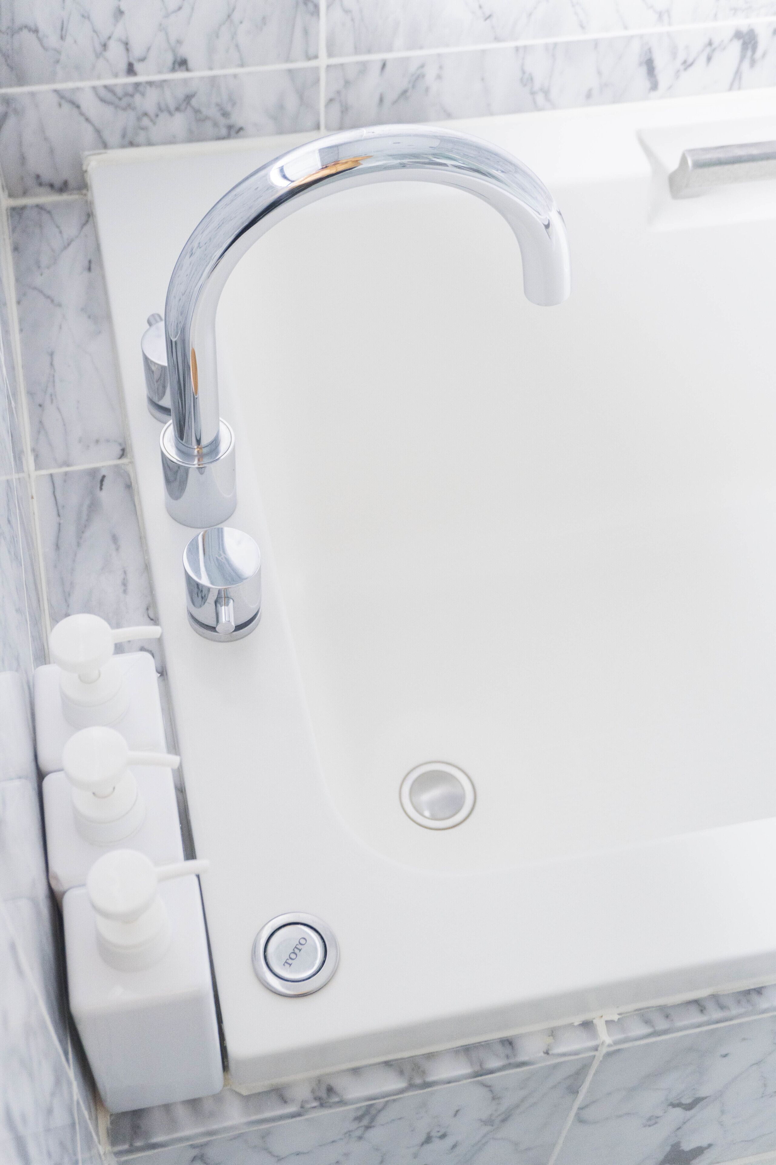 A modern bathroom with a white bathtub, chrome fixtures, and marble tiles.