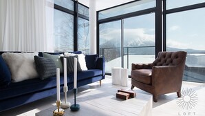 Uma sala de estar moderna com um sofá azul, uma poltrona marrom e uma vela branca sobre uma mesa de madeira.