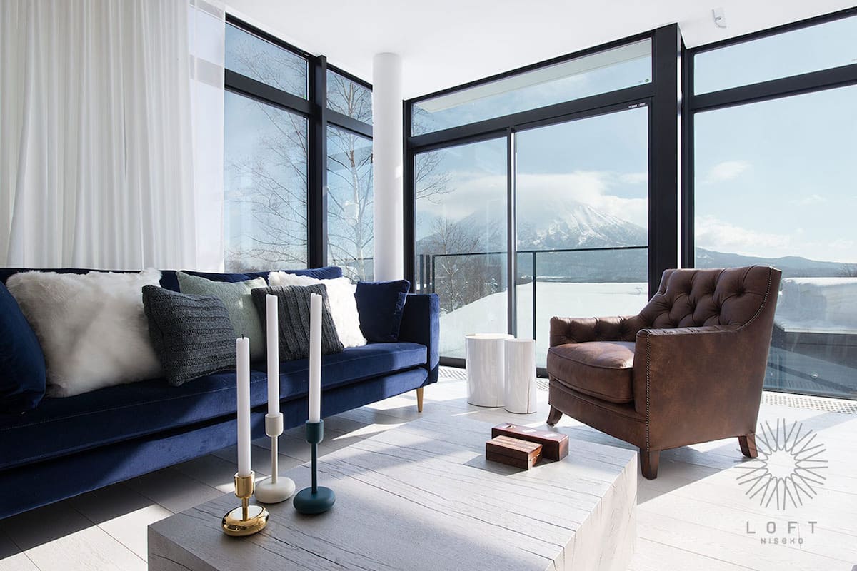 A modern living room with a blue sofa, a brown armchair, and a white candle on a wooden table.