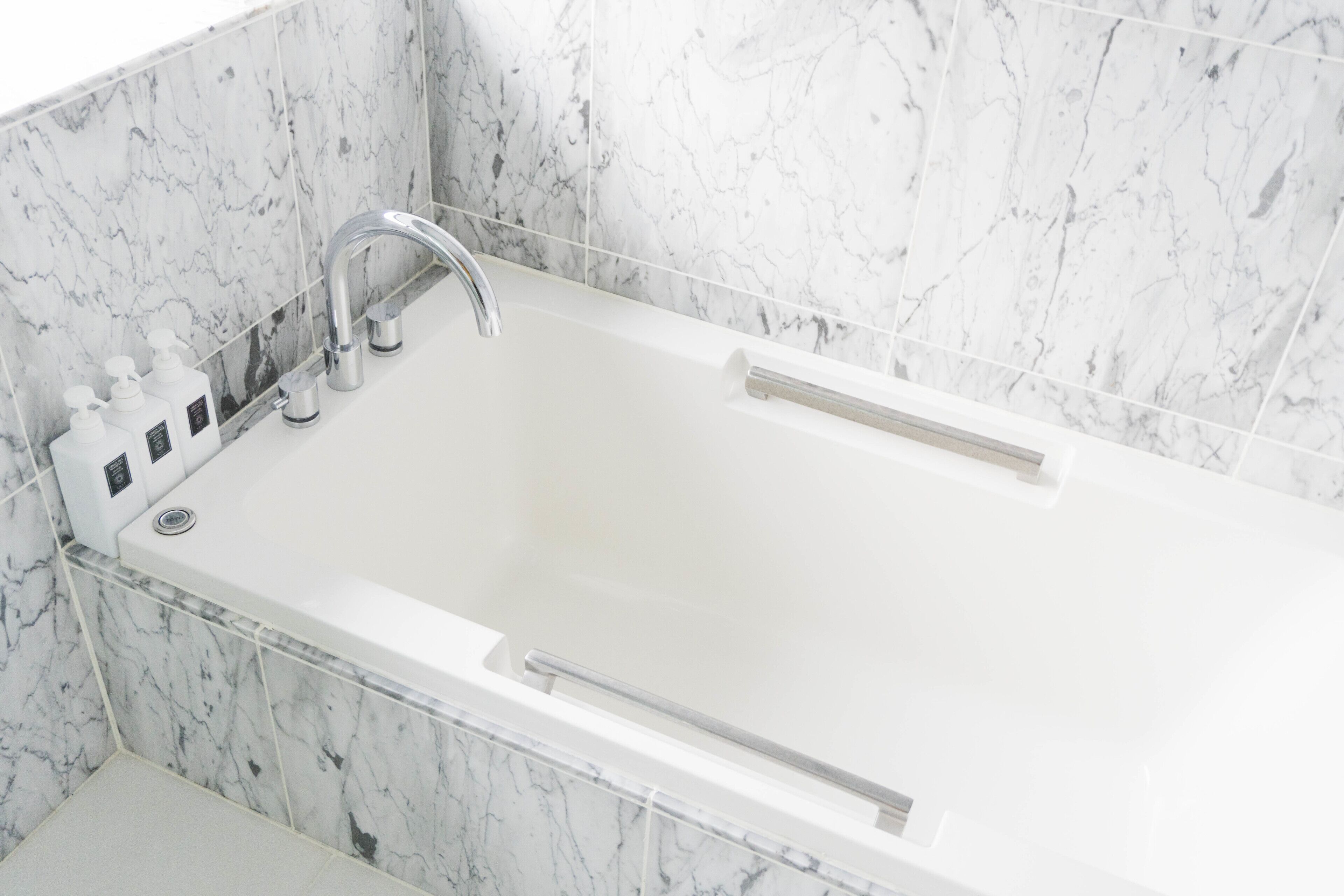 A modern bathroom with a white bathtub, chrome fixtures, and marble walls.
