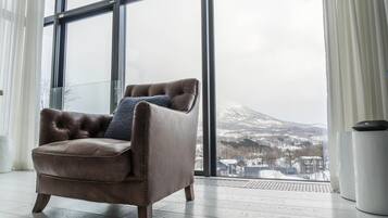 Un sillón de cuero marrón con un cojín azul en una habitación con ventanas amplias que dan a una montaña nevada.
