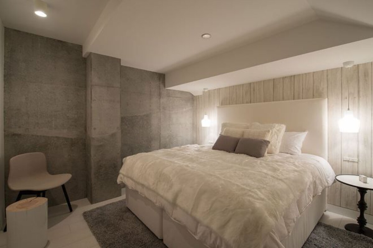 A modern bedroom with a large bed, a chair, and a small table.