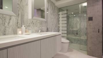 Un baño moderno con tocador de mármol, cabina de ducha con vidrio y un inodoro.